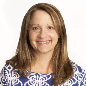 Headshot of Amy Lefkof on a white background. Amy is a middle-aged white woman wearing a blue patterned shirt. She is smiling and facing the camera.