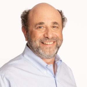 Headshot of David Tobias on a white background. David is a middle-aged white man, wearing a light blue shirt. His head is turned towards the camera, smiling, while his body is angled slightly away.