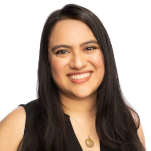 Headshot of Nadia Alia. Nadia is a Latina woman with straight black hair. She is looking at the camera smiling broadly. She is wearing a black blouse and a gold necklace.