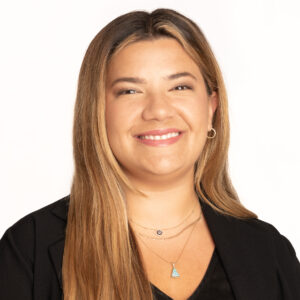 Headshot of Olivia Tow on a white background. Olivia is a young white woman wearing a black shirt with multiple chain necklaces and a pair of small hoop earrings. She is smiling and facing the camera.