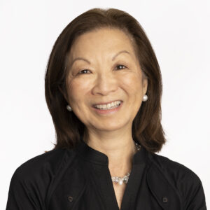Headshot of Teresa Law on a white background. Teresa is a middle-aged Asian woman, wearing a black shirt and pearl earrings. She is smiling and facing the camera.